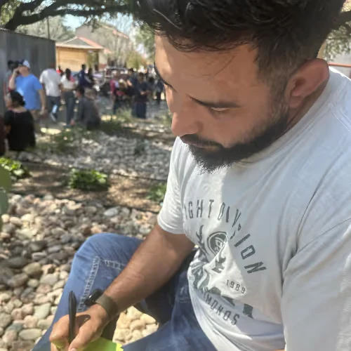 A guest in a gray T-shirt looking down and writing on a puzzle sheet outdoors in the Stockyards
