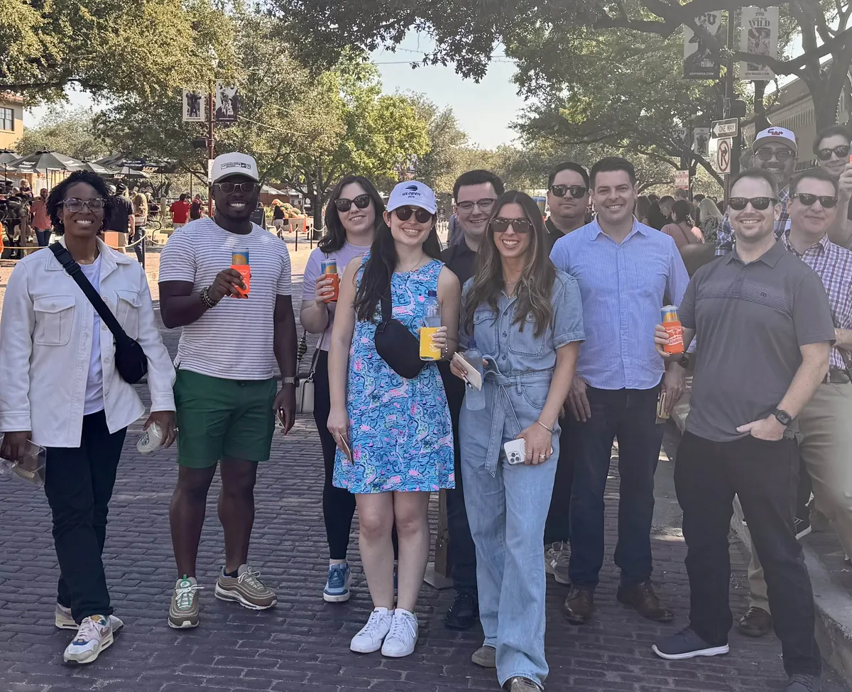 A group of a dozen guests smiling on a brick street in the Fort Worth Stockyards, several holding drinks in koozies