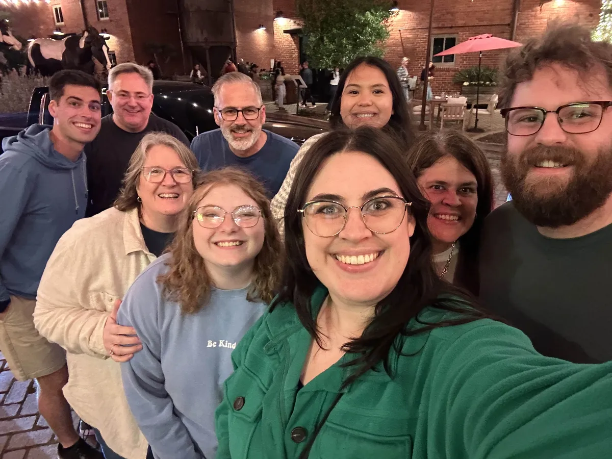 Nine friends crowding into a selfie at night in Mule Alley, with brick buildings and a cow statue behind them